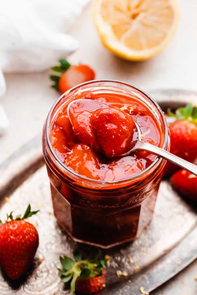 A jar of strawberry compote on a vintage metal tray with a spoon dipping in.