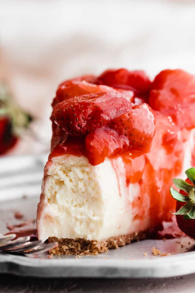 A close-up of a slice of the cheesecake with strawberry topping and a bite missing.