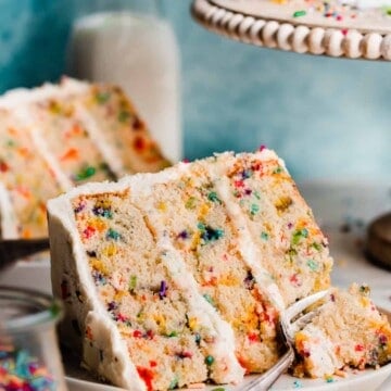 A slice of funfetti cake on a plate with a fork digging in.