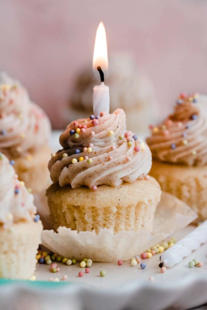 A mini vanilla cupcake with colorful sprinkles and a lit birthday candle.