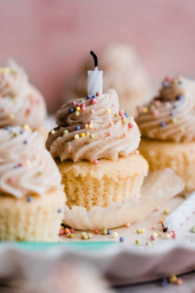 Mini vanilla cupcakes with brown butter frosting on a fluted plate, with rainbow sprinkles and birthday candles.