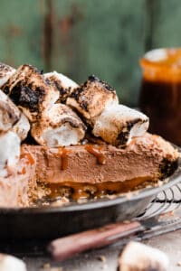 The sliced pie in a pie plate, with a visible cross section of the crust, caramel bottom, chocolate filling, & toasted marshmallows.