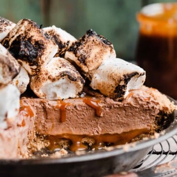 The sliced pie in a pie plate, with a visible cross section of the crust, caramel bottom, chocolate filling, & toasted marshmallows.