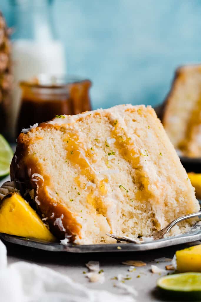 A slice of pina colada cake on a plate, with a few bites missing.