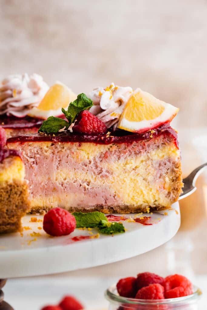 A close-up on a slice of cheesecake with visible swirls of raspberry and lemon bater. 