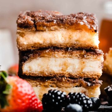 A stack of three sopapilla cheesecake bars drizzled with honey.