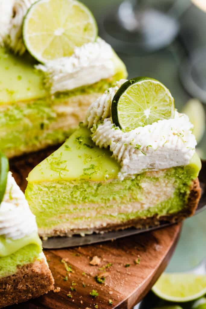 A slice of the key lime cheesecake on a cake stand being lifted out.