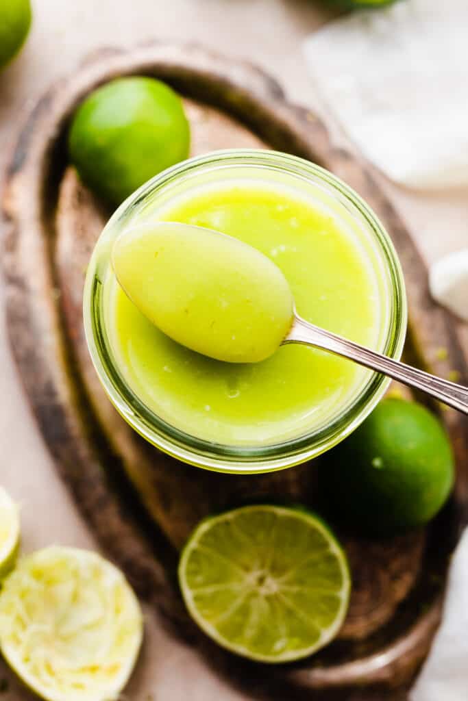 A close-up of a spoon resting on a jar of lime curd.
