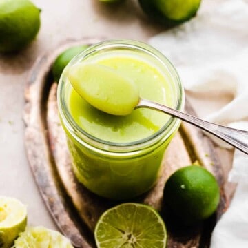 A spoon resting on a jar of bright green lime curd.