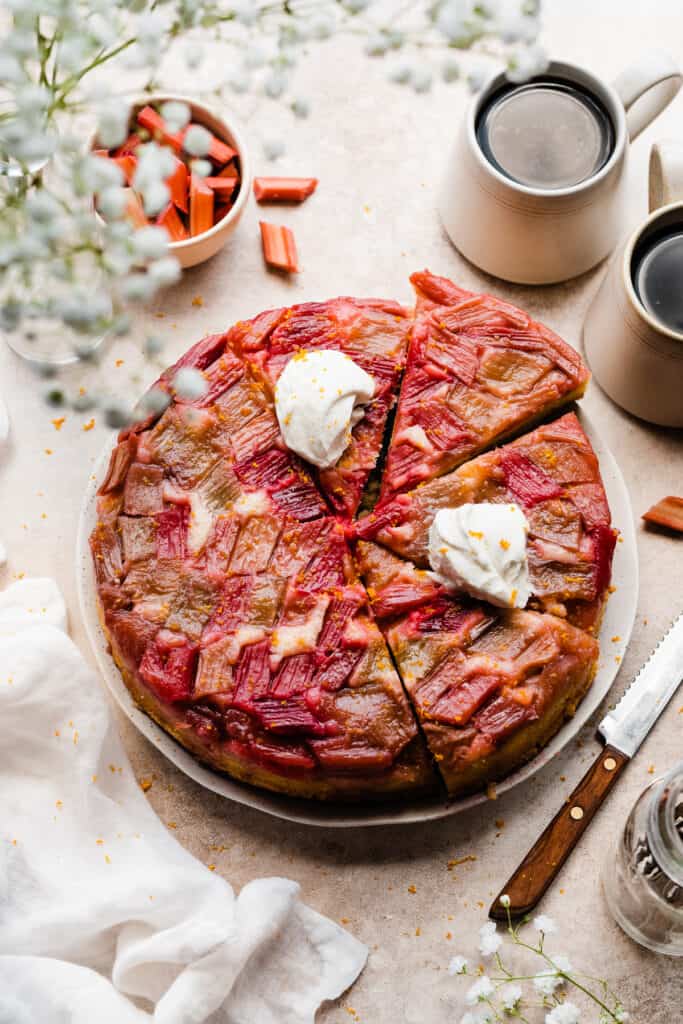 Sliced rhubarb cake on a platter, with dollops of whipped cream on the slices.