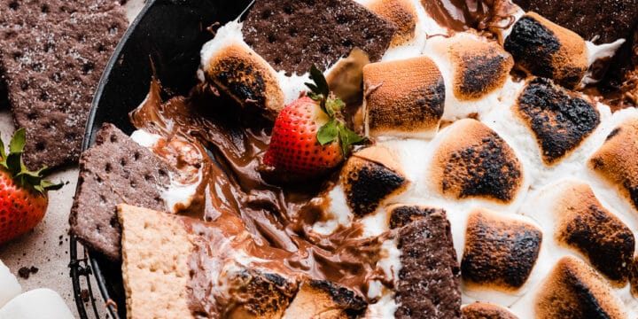 A skillet of s'mores dip with graham crackers scooping out the melty dip.