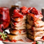 A stack of strawberry pancakes with a section missing, topped in strawberry compote.