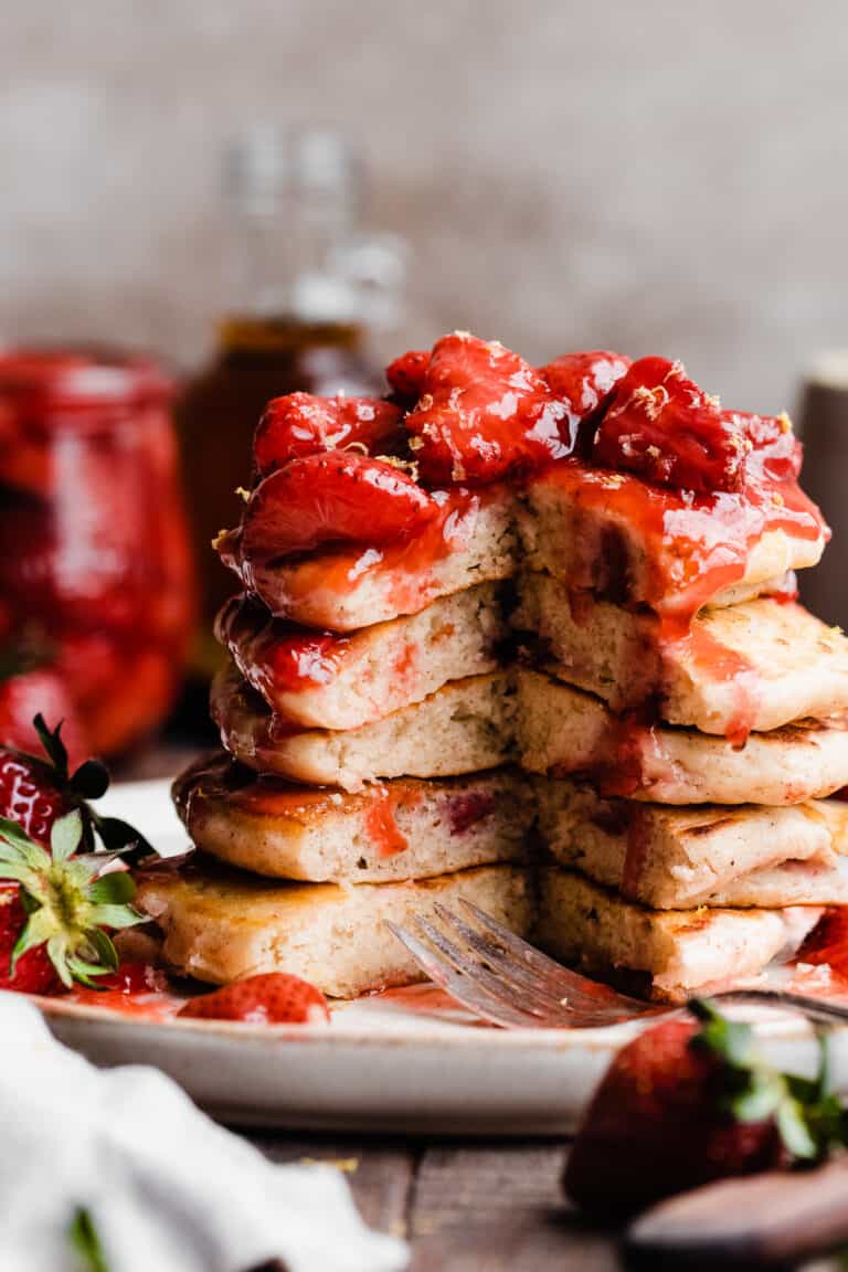 A stack of strawberry pancakes with a section missing, topped in strawberry compote.
