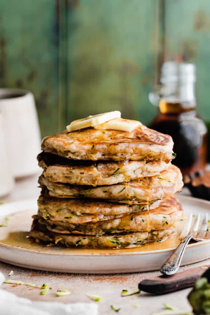A stack of zucchini pancakes dripping with maple syrup.