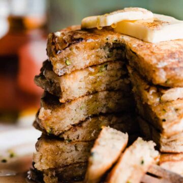 A stack of sliced open zucchini pancakes with maple syrup dripping down.