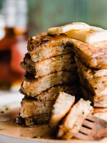 A stack of sliced open zucchini pancakes with maple syrup dripping down.