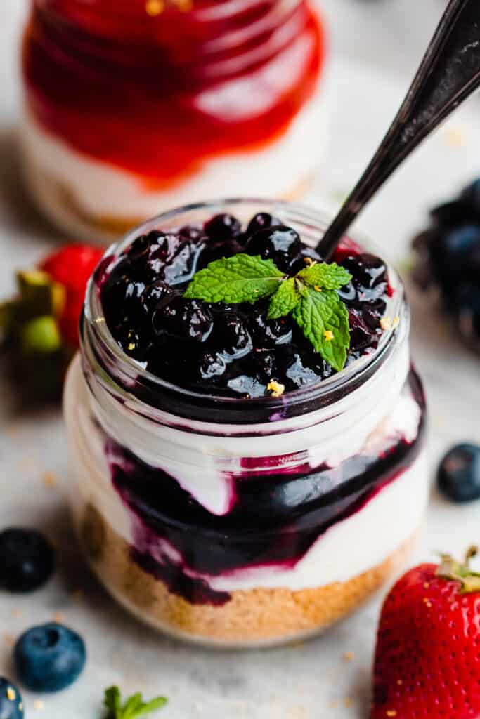 A close-up on a jar of a mini cheesecake with blueberry topping.