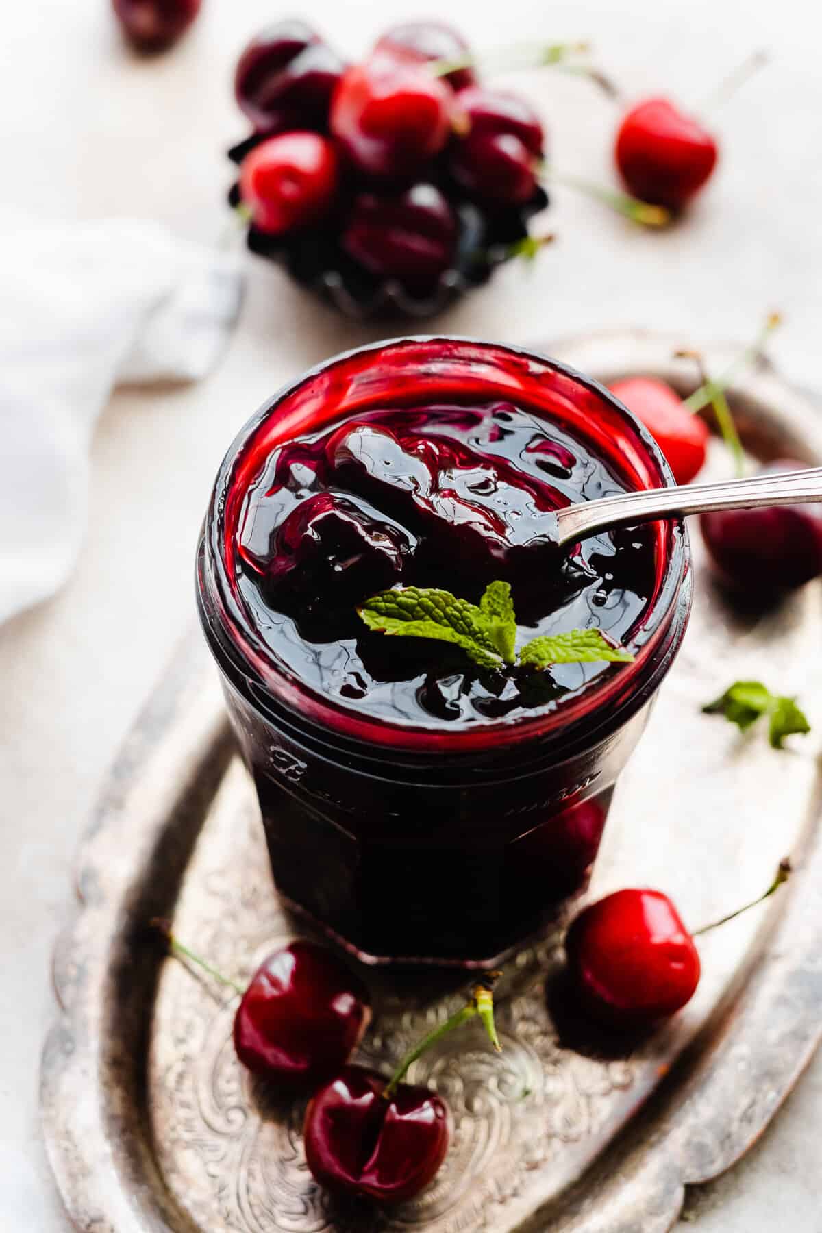 A jar of cherry compote with a spoon going in.