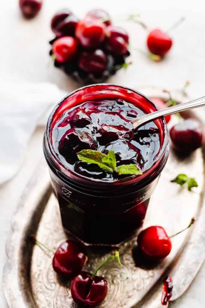 A jar of cherry compote with a spoon going in.