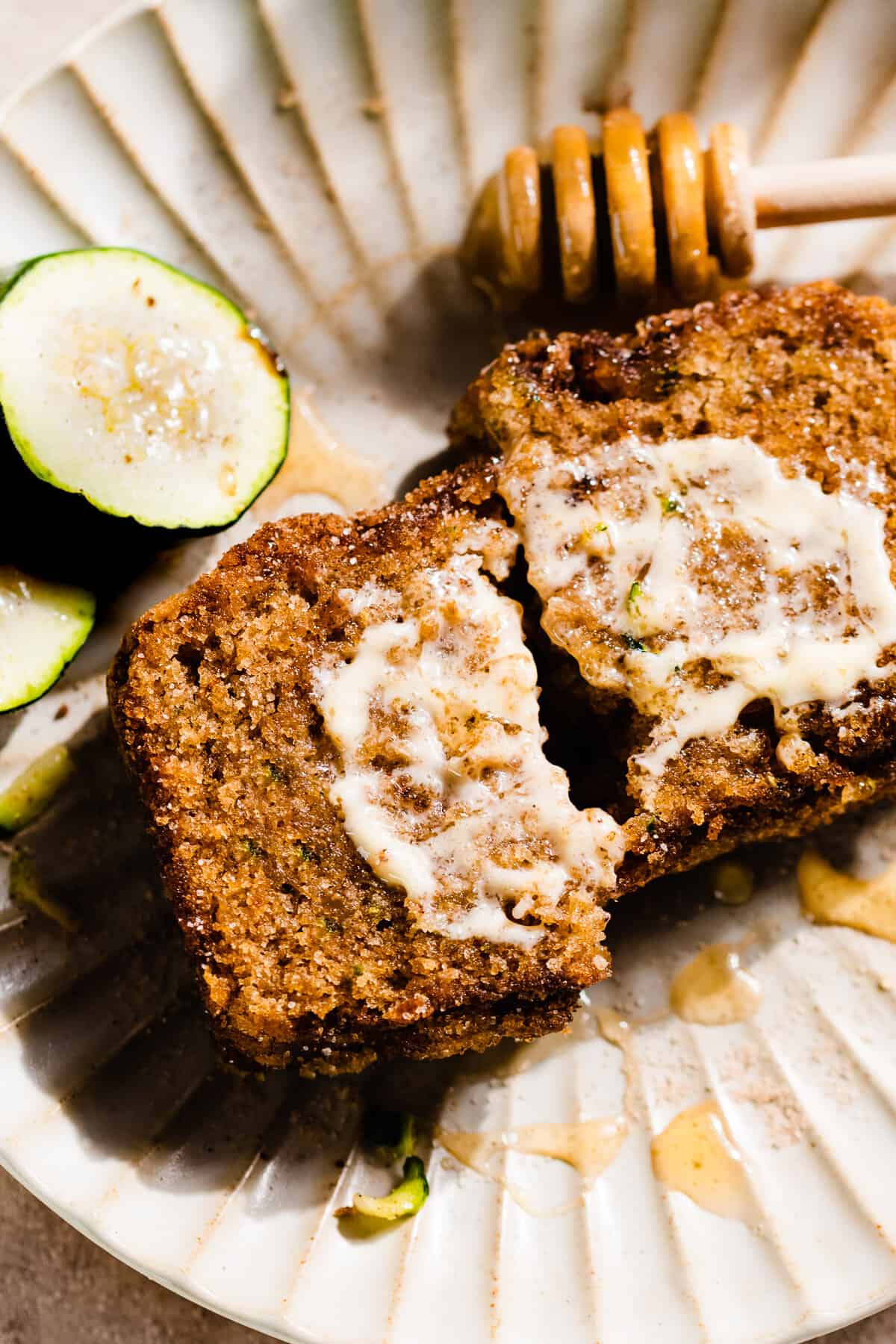 Two halves of a slice of zucchini bread on a plate, with a swoop of honey butter.