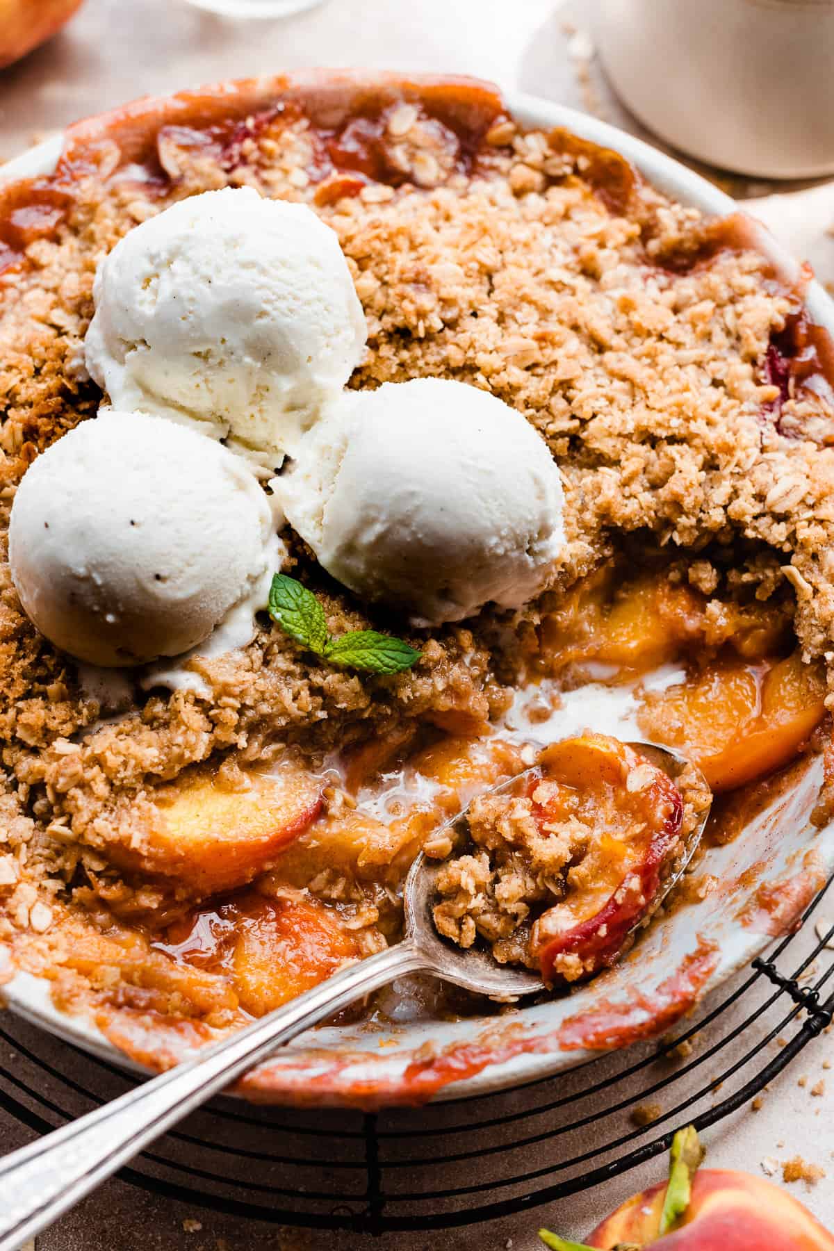 A baking dish of peach crisp topped with scoops of vanilla ice cream.