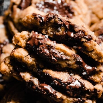 A close-up on a stack of four brown butter chocolate chip cookie halves, showing their gooey insides.