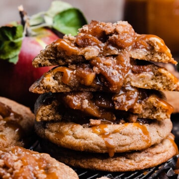 A stack of caramel apple pie cookies with a few broken in half to show the chewy cookies and apple filling.