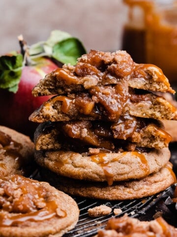 A stack of caramel apple pie cookies with a few broken in half to show the chewy cookies and apple filling.