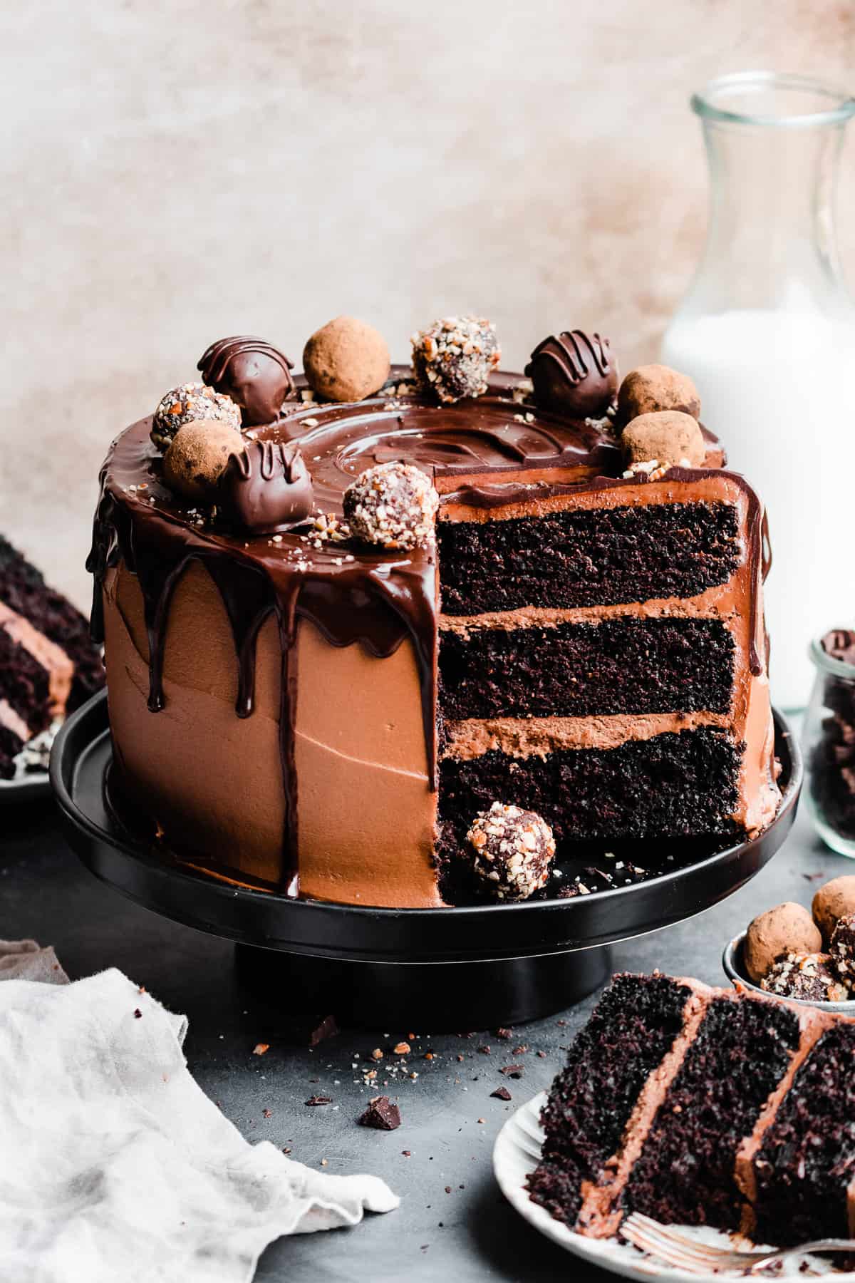 The sliced chocolate truffle cake topped with chocolate drip and truffles, with slices on plates.