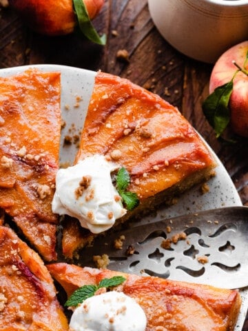 A close-up on slices of the peach upside down cake on a plate, topped with whipped cream.