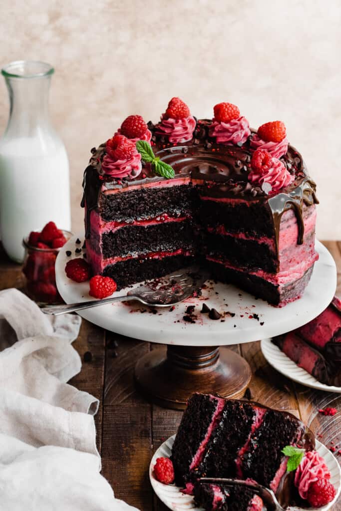 The sliced chocolate raspberry cake on a cake stand, topped with frosting swirls and raspberries.