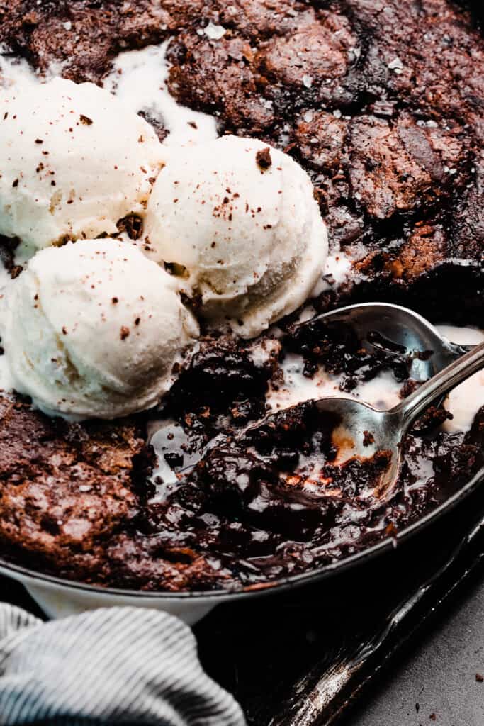A close-up of two spoons digging into the pan of chocolate cobbler.