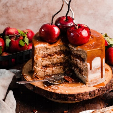 A sliced open caramel apple cake with caramel drip, apple filling, and candy apples on top.