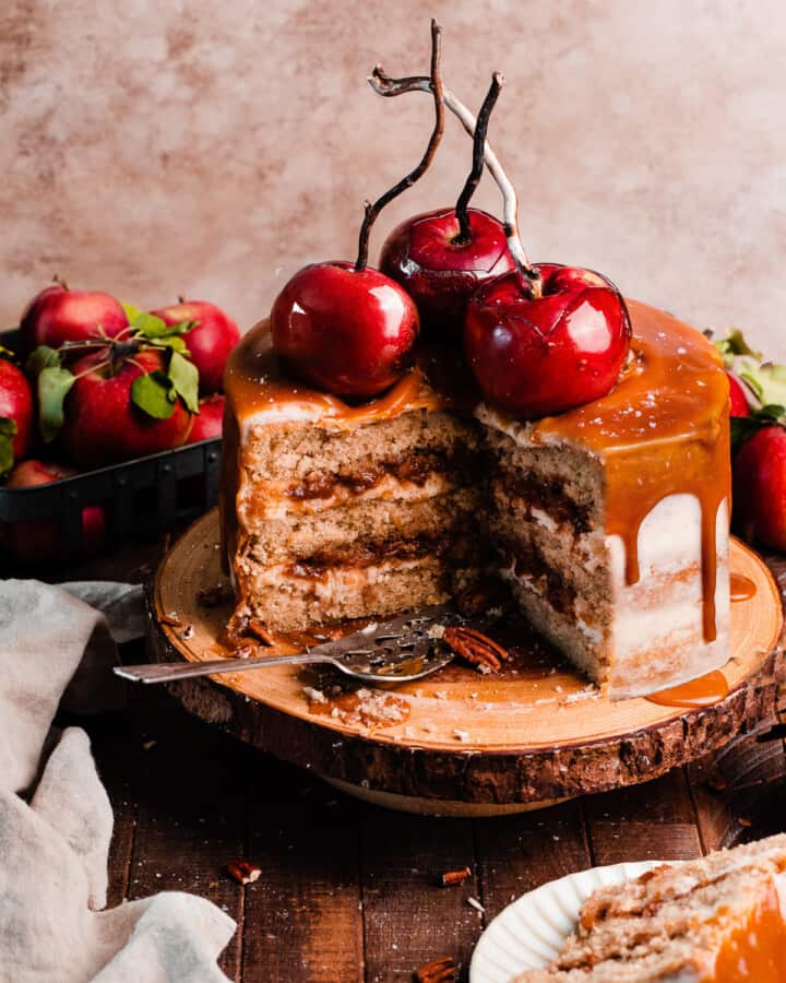 A sliced open caramel apple cake with caramel drip, apple filling, and candy apples on top.