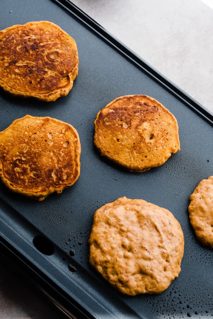 Pumpkin pancakes cooking on a griddle.
