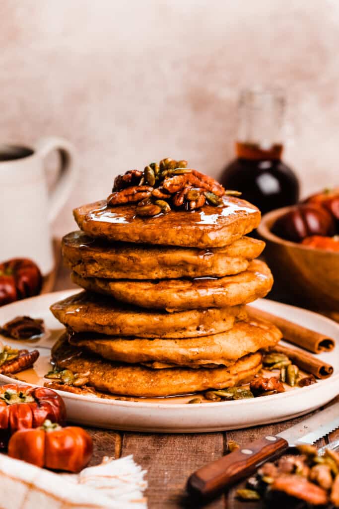 A stack of the pumpkin pancakes topped with candied pecans and maple syrup.