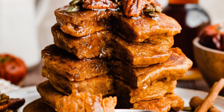 A tall stack of pumpkin pancakes topped with candied pecans and real maple syrup.