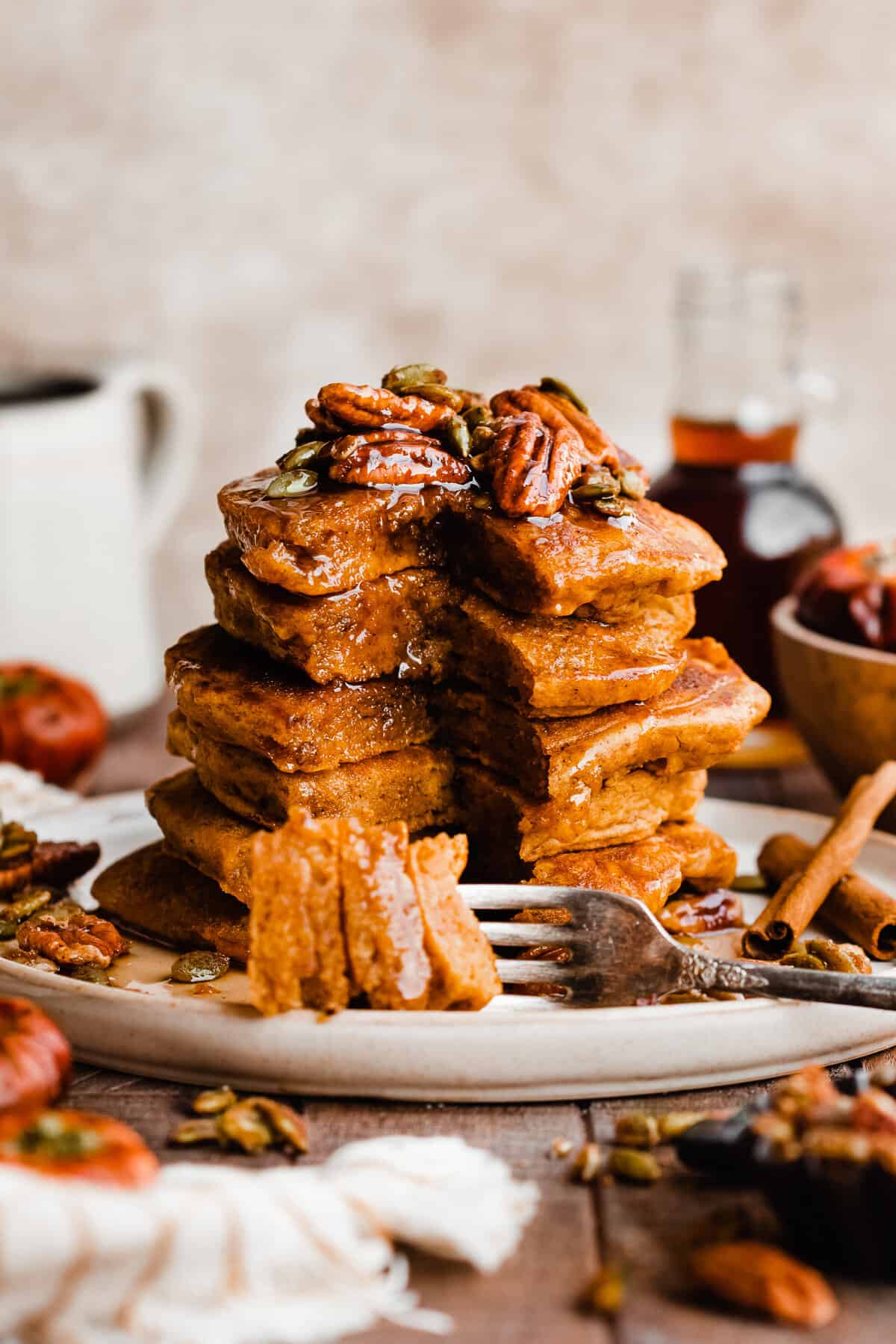 A tall stack of pumpkin pancakes topped with candied pecans and real maple syrup.
