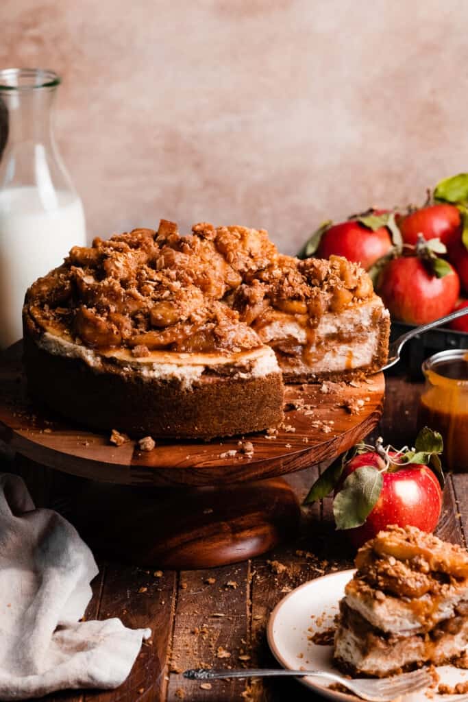 The sliced apple crumble cheesecake on a cake stand, with apple filling, crumble, and caramel on top.