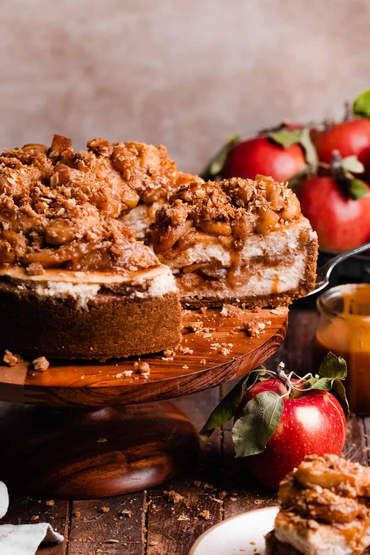 The sliced apple crumble cheesecake on a cake stand, with apple filling, crumble, and caramel on top.