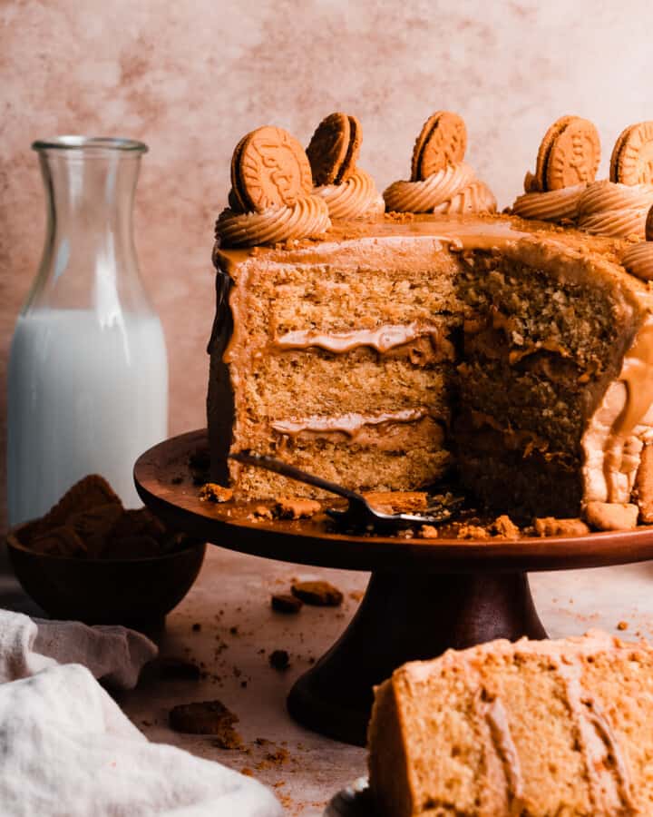 The sliced open biscoff cake on a cake stand, with swirls of frosting and biscoff cookies on top of the cake.