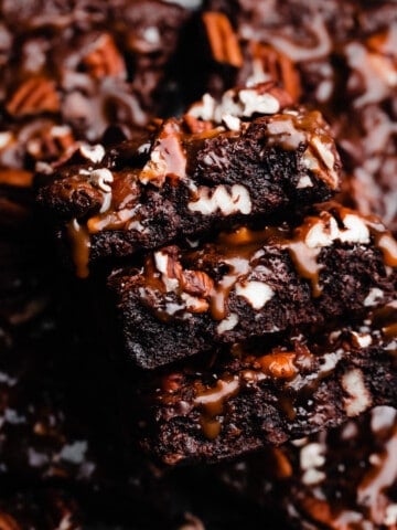 A close-up on a stack of turtle brownies with salted caramel sauce dripping down the sides.