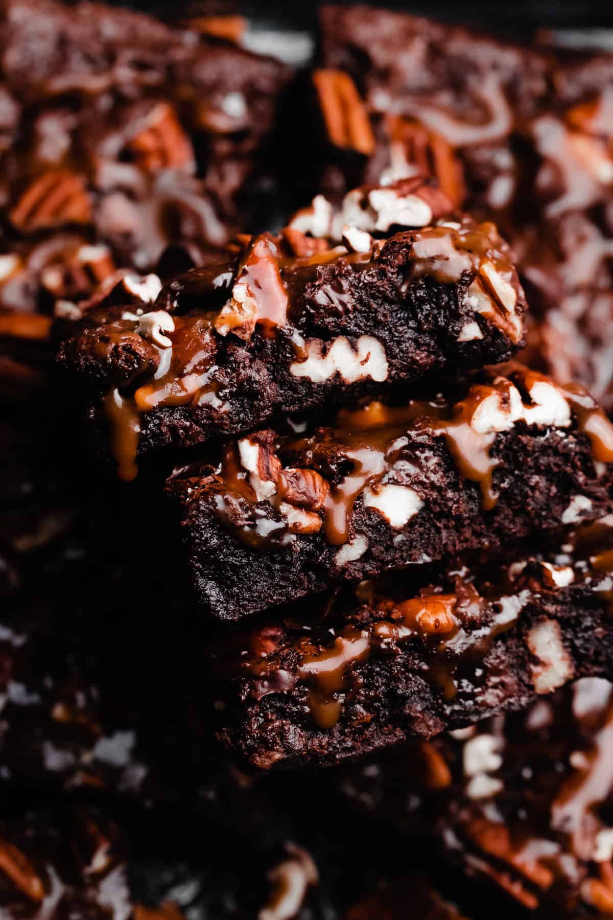 A close-up on a stack of turtle brownies with salted caramel sauce dripping down the sides.