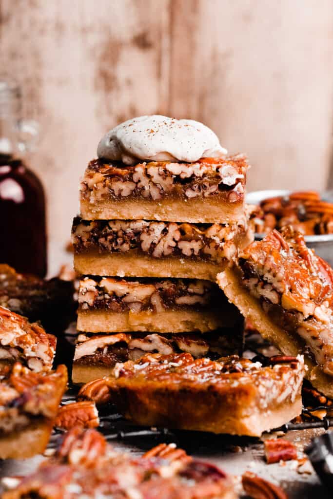 A stack of pecan pie bars topped with a dollop of whipped cream.