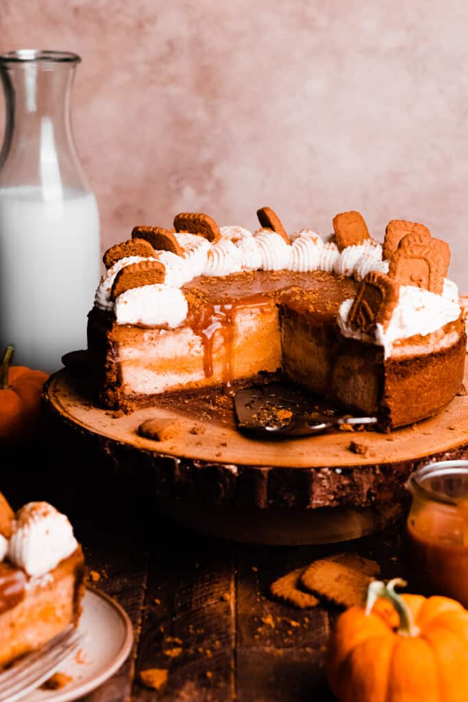 The sliced open pumpkin pie cheesecake on a cake stand, topped with caramel sauce and whipped cream.