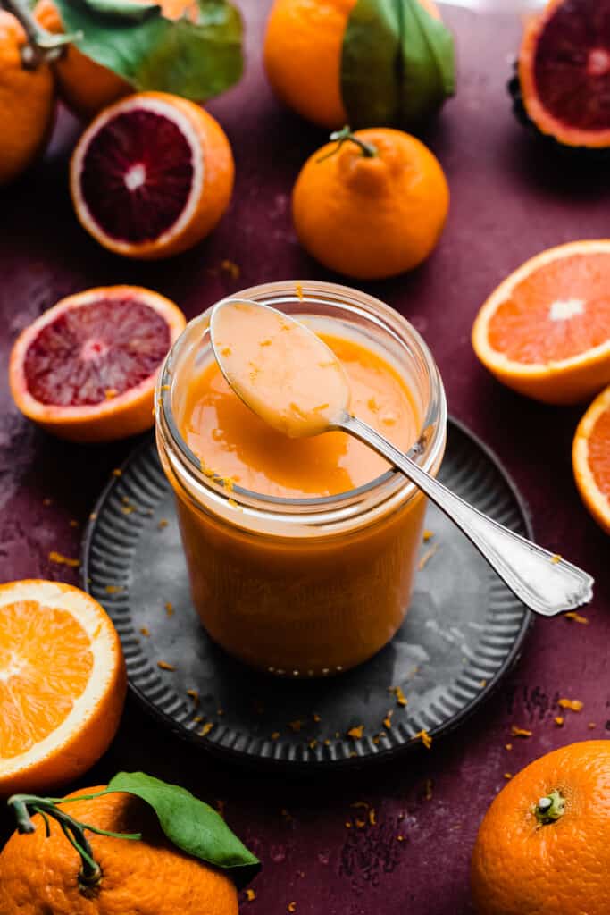 A jar of orange curd with a spoonful of orange curd balanced on top.