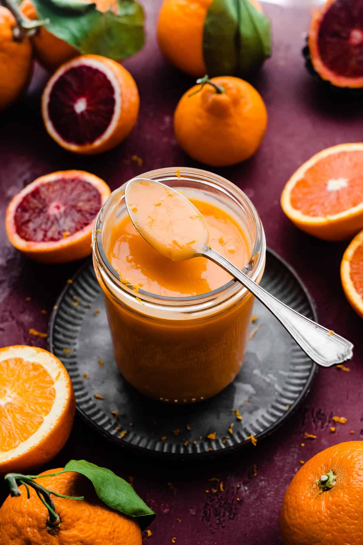 A spoonful of orange curd resting on top of a jar of the silky orange curd.