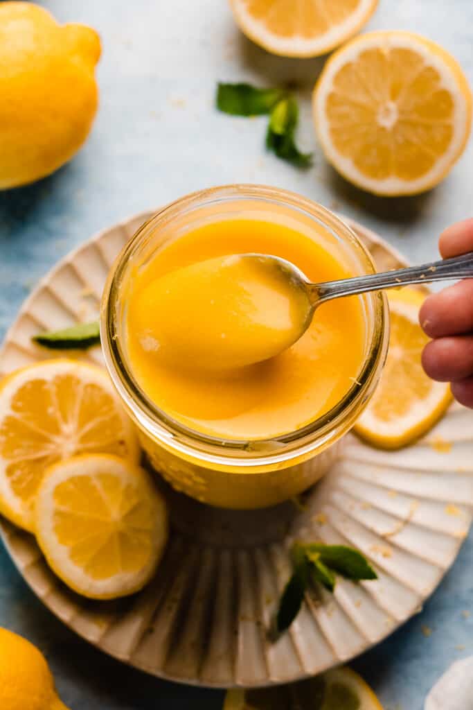 A spoon dipping into a jar of silky lemon curd.
