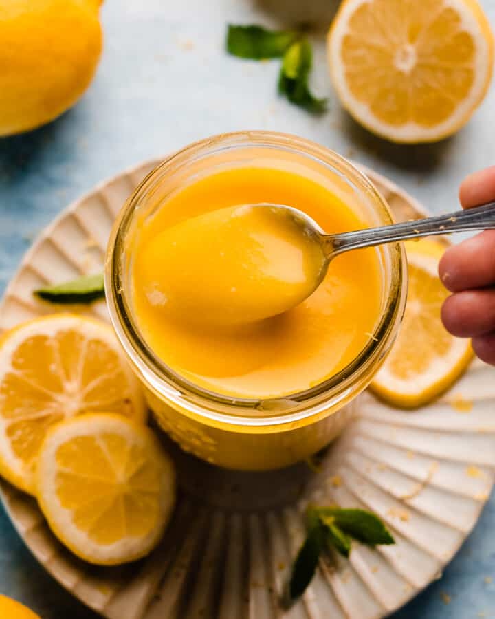 A spoon dipping into a jar of silky lemon curd.