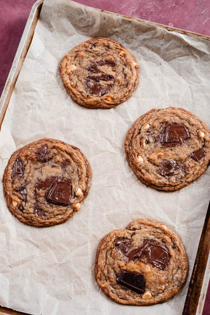 Four thin and chewy cookies on a cookie sheet, after the final pan bang.